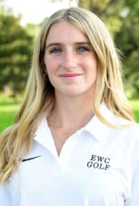 A young woman with long blonde hair and blue eyes, wearing a white collared shirt embroidered with EWC GOLF, stands outdoors in front of a blurred green background.