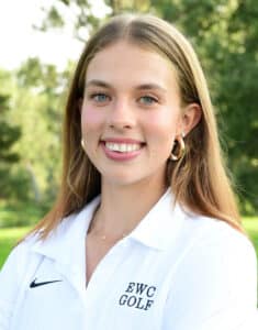A young woman with long light brown hair, wearing hoop earrings and a white EWC Golf polo shirt, smiles outdoors with trees and greenery in the background.