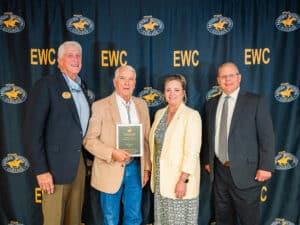 Four people standing in front of an Eastern Wyoming College backdrop, with the man second from left holding an award plaque.